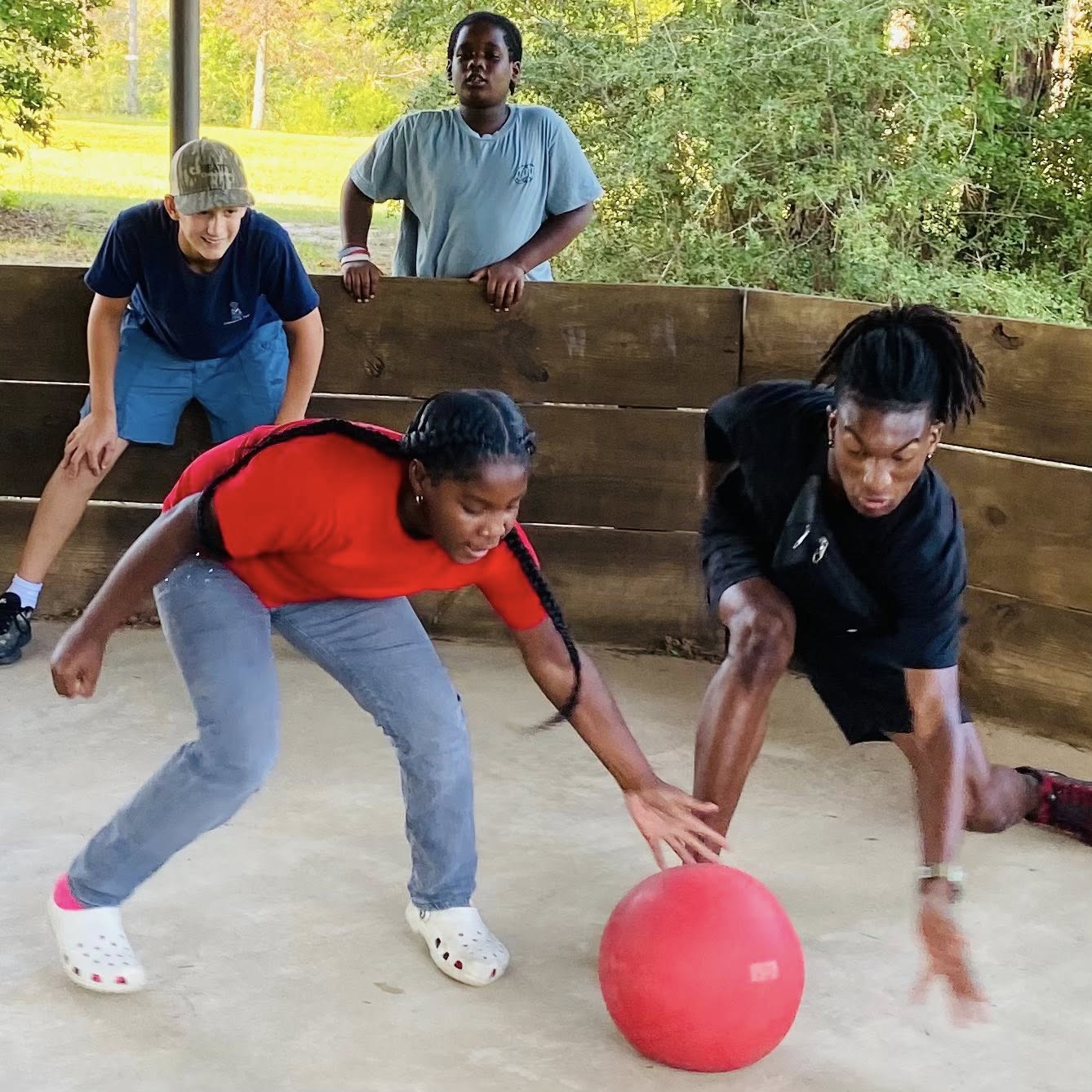 Two kids bending to get a red ball.
